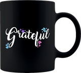 Eleven ounce black coffee mug with the word Grateful written on it with blue purple and pink flowers